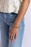 Person wearing a floral top, blue jeans, and gold bracelet