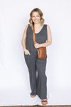 Woman wearing a gray jumpsuit holding a brown leather bag 