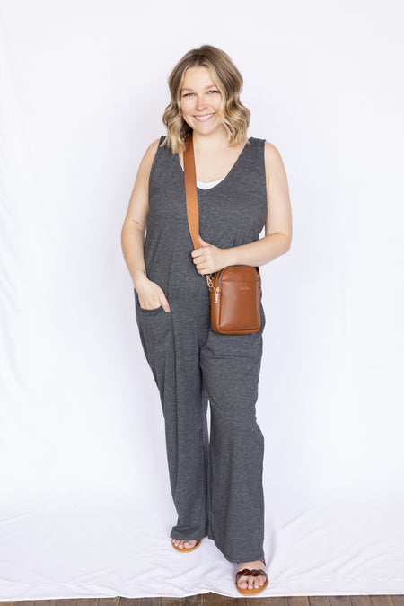 Woman wearing a gray jumpsuit holding a brown leather bag 