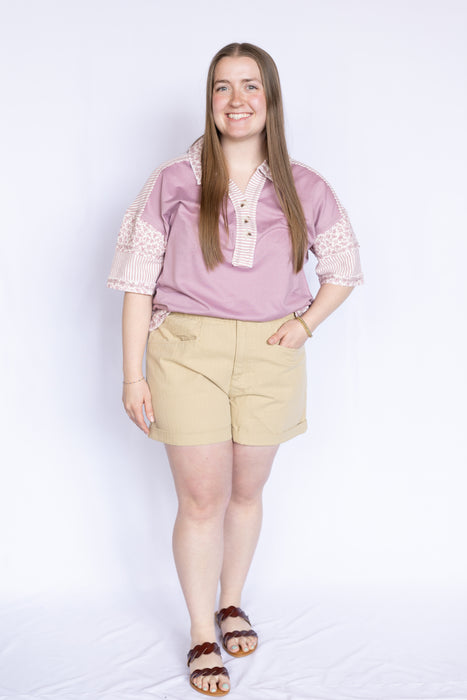 Woman wearing a pink blouse with floral trim and beige shorts 