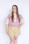 Woman wearing a pink blouse with floral trim and beige shorts 