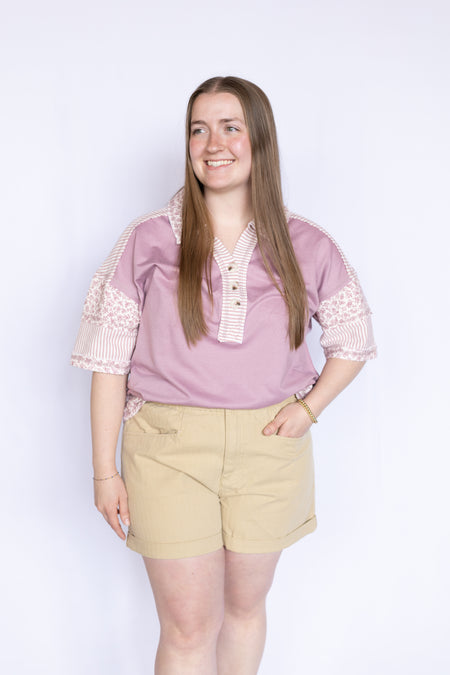 Woman wearing a pink blouse with floral trim and beige shorts 