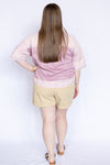 Woman wearing a pink blouse with floral trim and beige shorts 