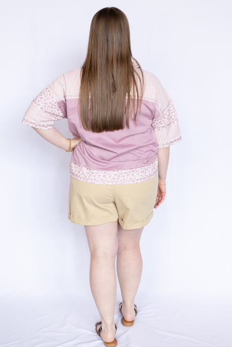 Woman wearing a pink blouse with floral trim and beige shorts 