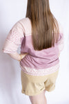 Woman wearing a pink blouse with floral trim and beige shorts 
