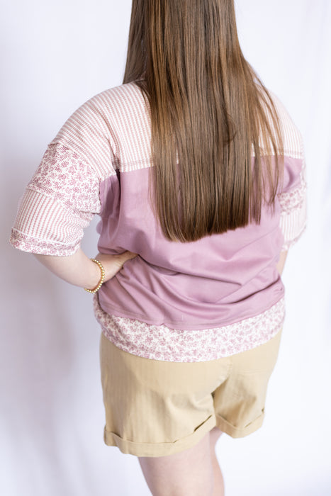 Woman wearing a pink blouse with floral trim and beige shorts 