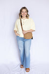 Woman wearing a light yellow top and blue jeans, holding a brown bag 