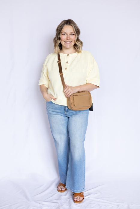 Woman wearing a light yellow top and blue jeans, holding a brown bag 