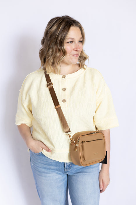 Woman wearing a yellow shirt and blue jeans with a brown crossbody bag 