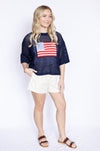Woman wearing a navy blue top with an American flag design and white shorts 