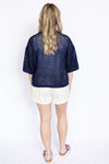 Person wearing a navy blue open-knit top over a white top and shorts 