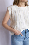 Person wearing a white sleeveless top with lace details and blue jeans 