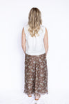 Person wearing a white sleeveless top and brown floral skirt 