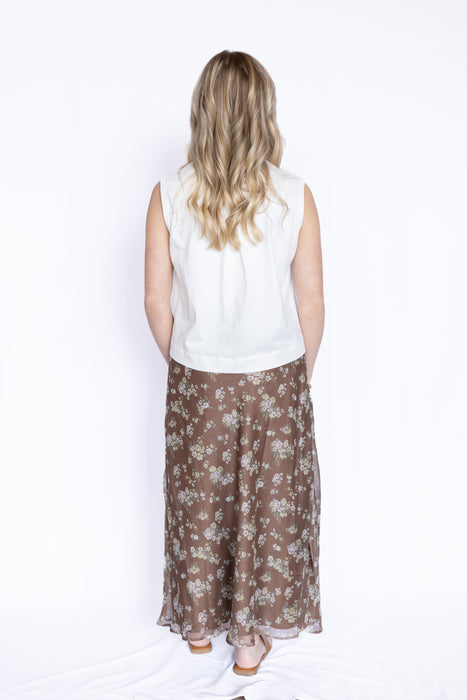 Person wearing a white sleeveless top and brown floral skirt 