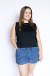 Woman wearing a black sleeveless top and blue denim shorts 