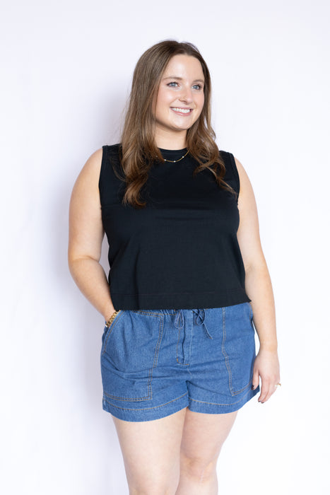 Woman wearing a black sleeveless top and blue denim shorts 