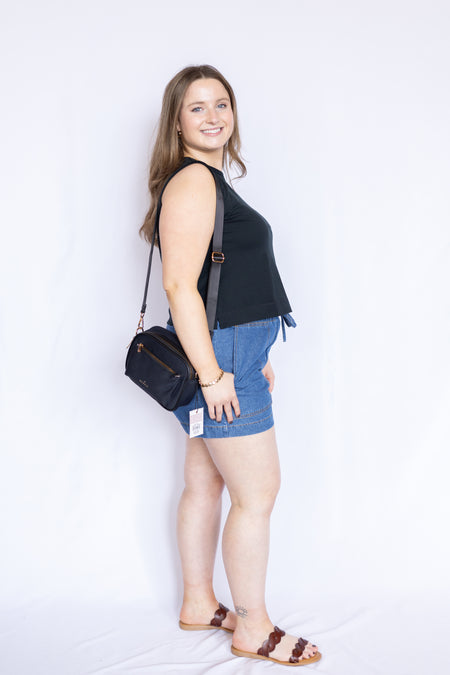 Woman wearing a black sleeveless top and denim shorts with a black handbag 