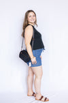 Woman wearing a black sleeveless top and denim shorts with a black handbag 