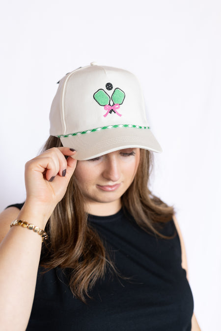Person wearing a cap with a tennis racket and pink ribbon design 