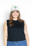Woman wearing a black sleeveless top and blue jeans with a white cap with a green and pink pickleball design 