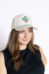 Woman wearing a beige cap with a green and pink pickleball design 
