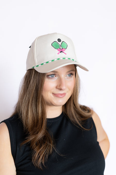 Woman wearing a beige cap with a green and pink pickleball design 