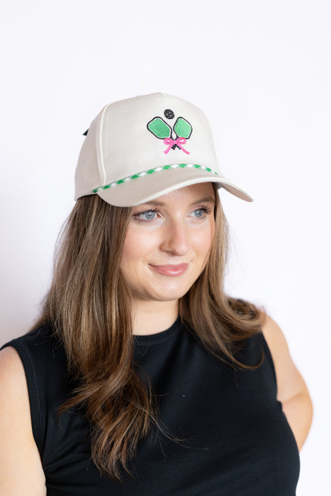 Woman wearing a beige cap with a green and pink pickleball design 