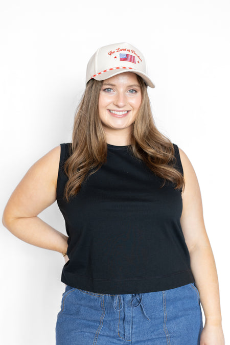 Woman wearing a black sleeveless top and blue jeans with a white cap on a white background