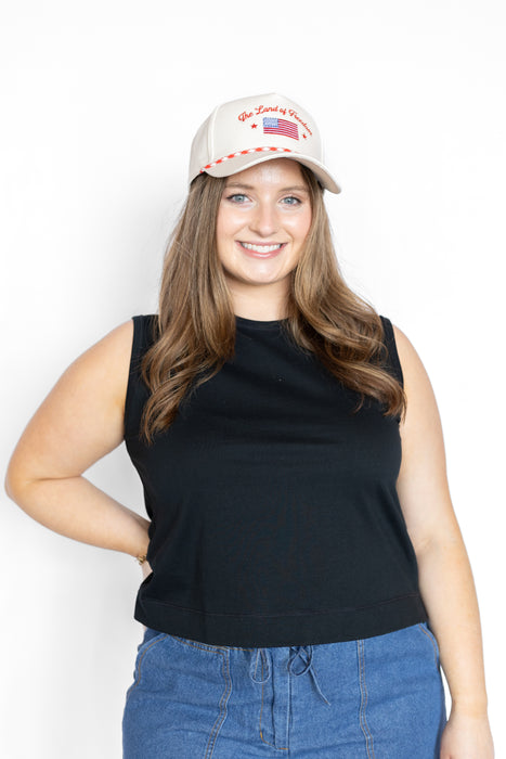 Woman wearing a black sleeveless top and blue jeans with a white cap on a white background