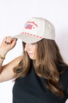 Woman wearing a beige cap with red and white text and an American flag hat