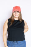 Woman wearing a black sleeveless top and blue jeans with a red smiley face cap 