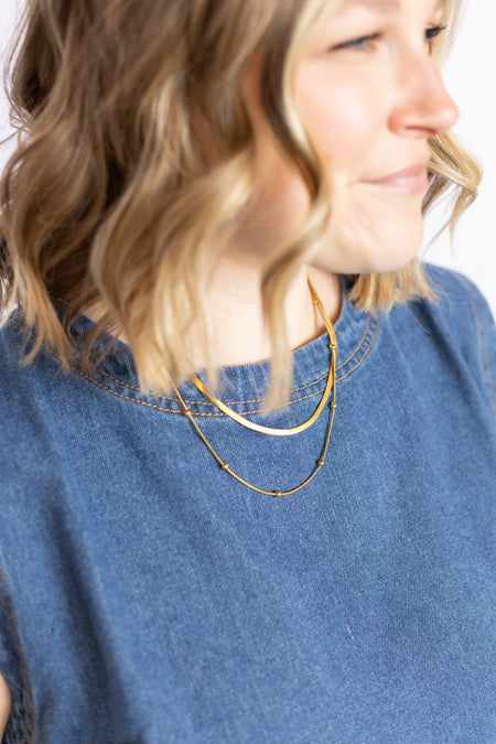 Woman wearing a gold necklace with a blue shirt 
