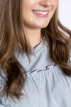 Close-up of a person wearing a light gray blouse and pearl necklace