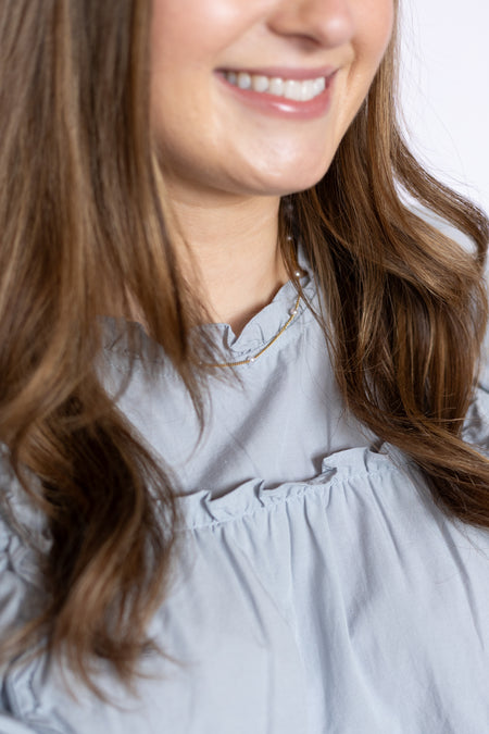 Close-up of a person wearing a light gray blouse and pearl necklace