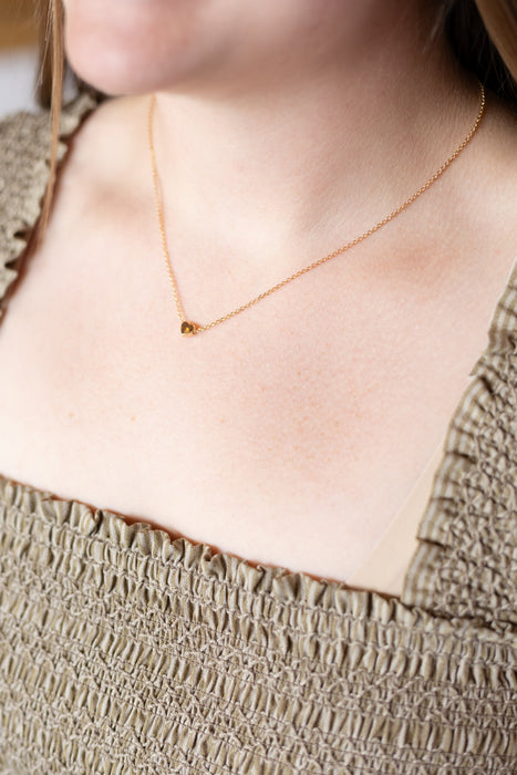 Close-up of a person wearing a gold heart necklace 