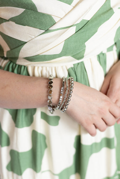 Close-up of a person wearing multiple bracelets on a green and white patterned fabric dress