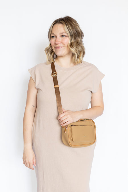 Woman holding a tan crossbody bag 