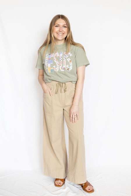 Woman wearing a green t-shirt with embroidered Jesus text and beige pants 