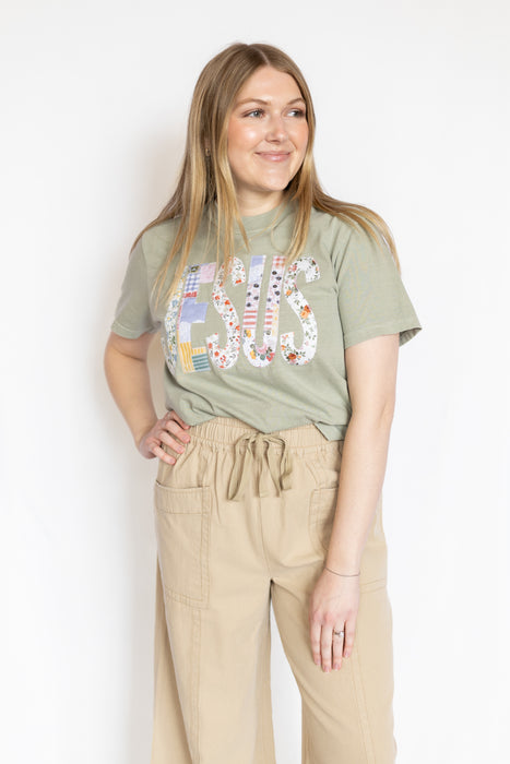 Woman wearing a green t-shirt with embroidered Jesus text and beige pants 