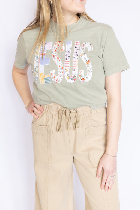 Woman wearing a green t-shirt with embroidered Jesus text and beige pants 