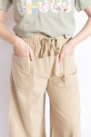 Person wearing a green t-shirt with colorful text and beige pants 