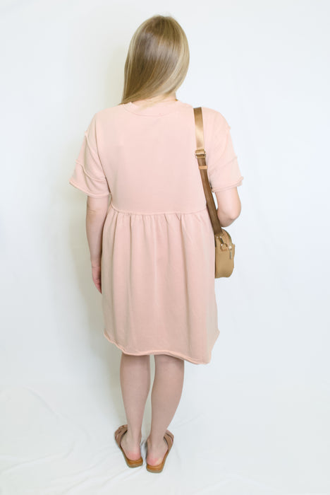Woman wearing a pink dress holding a beige handbag 