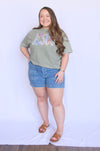 Woman wearing a green t-shirt with colorful graphics and denim shorts 