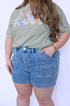 Person wearing a green t-shirt with colorful text and blue denim shorts 