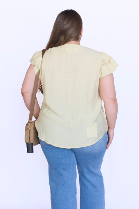 Woman wearing a light yellow blouse and blue jeans with a beige bag 