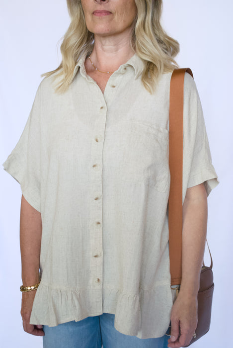 Woman wearing a beige button-up shirt and blue jeans with a brown leather bag