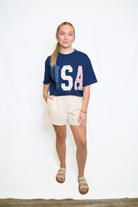 Woman wearing a blue t-shirt with 'USA' letters and beige shorts 