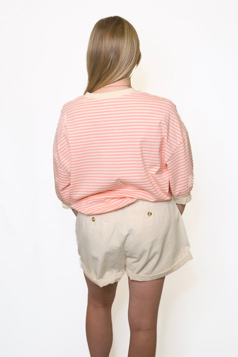 Person wearing a pink striped sweater and beige shorts 