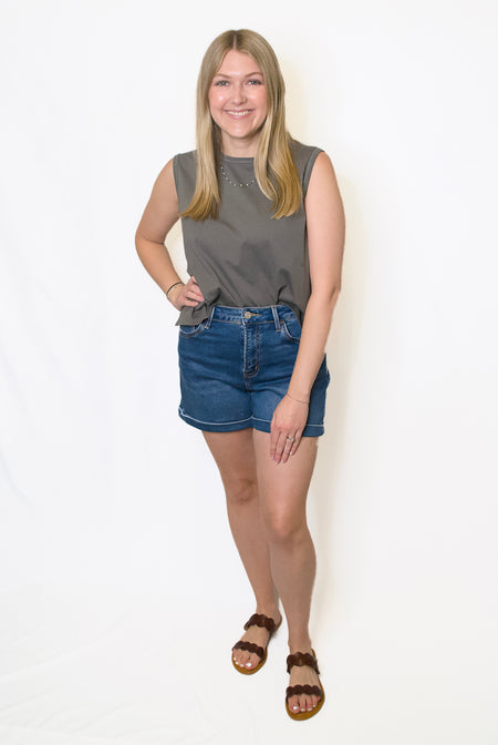 Woman wearing a gray sleeveless top and blue denim shorts 