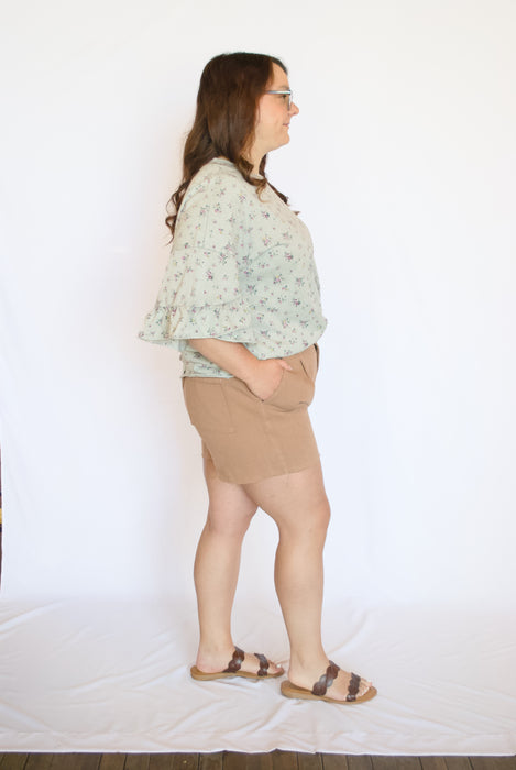 Woman wearing a light grey patterned blouse and beige shorts 
